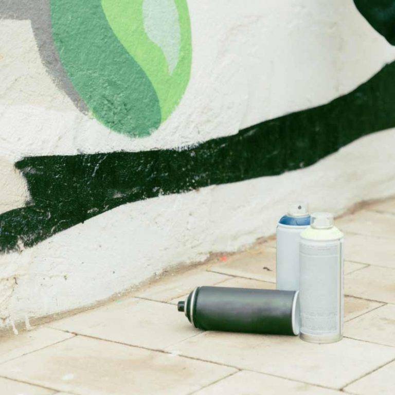 Zwei Spraydosen vor verschmutzter Wand zeigen Reinigungskonzepte Freibergs Expertise in effizienter Graffitientfernung.
