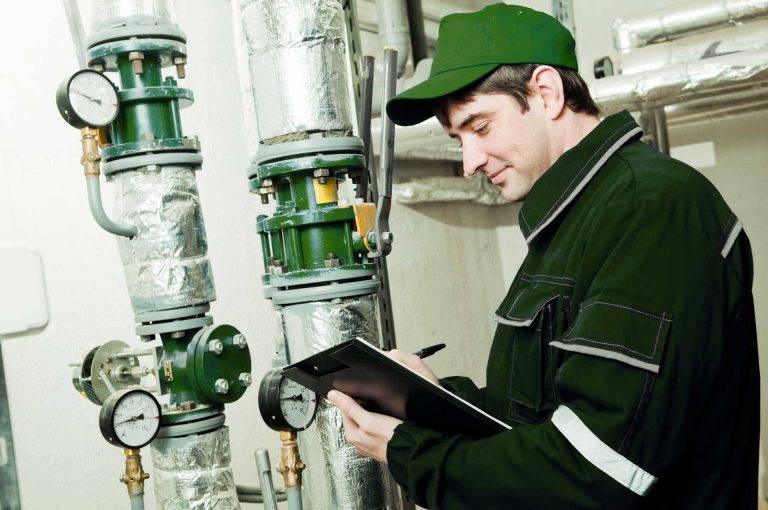 Mitarbeiter von Reinigungskonzepte Radeberg in grüner Arbeitskleidung prüft im Maschinenraum Daten auf einem Klemmbrett.