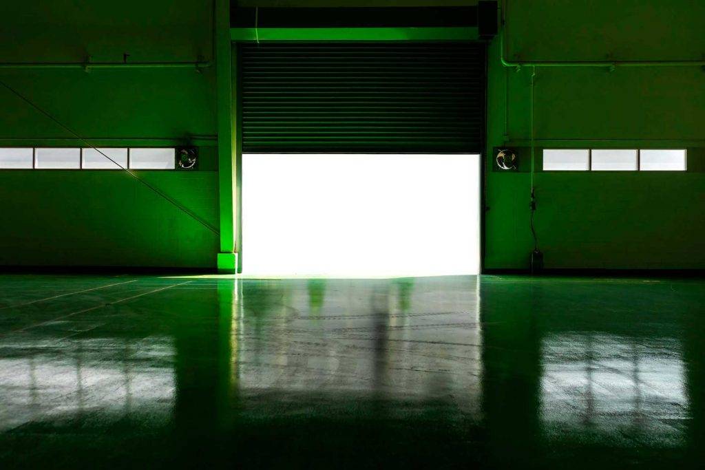 Ein halb geöffnetes Rolltor einer Tiefgarage, im grünem Licht. Reinigungskonzepte übernimmt die Tiefgaragenreinigung.
