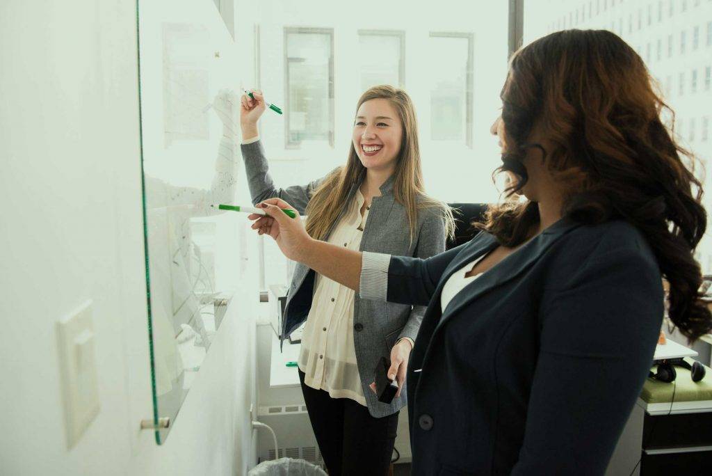 Zwei Mitarbeiterinnen von Reinigungskonzepte Chemnitz planen lächelnd vor Whiteboard einen individuellen Reinigungsplan.