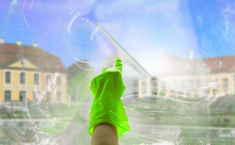Ein Mitarbeiter von Reinigungskonzepte säubert mit Glasabzieher & grünen Handschuhen ein Fenster mit Blick auf Heidenau.