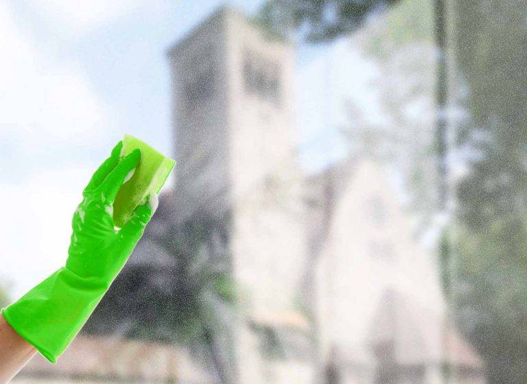 Ein Profi von Reinigungskonzepte putzt mit einem Schwamm ein Fenster. Im Hintergrund kann man unscharf Bochum erkennen.