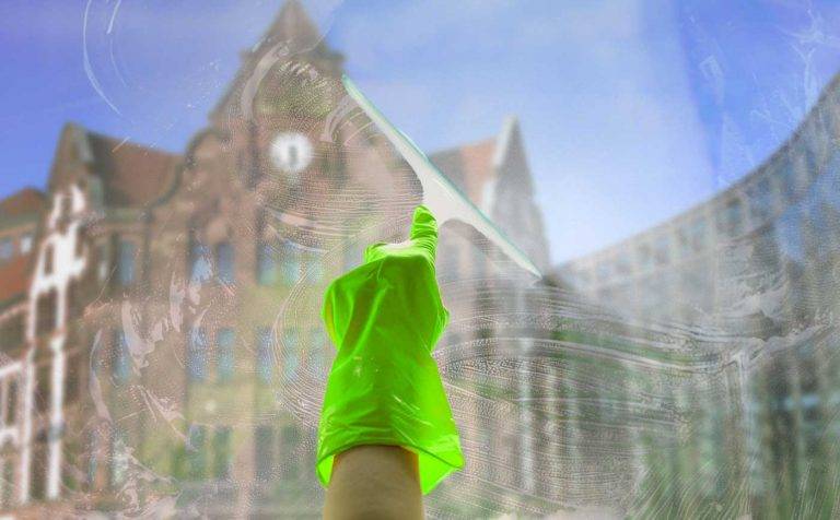 Ein Mitarbeiter von Reinigungskonzepte putzt eine Fensterscheibe. Hinter dem Glas kann man unscharf Dortmund erkennen.
