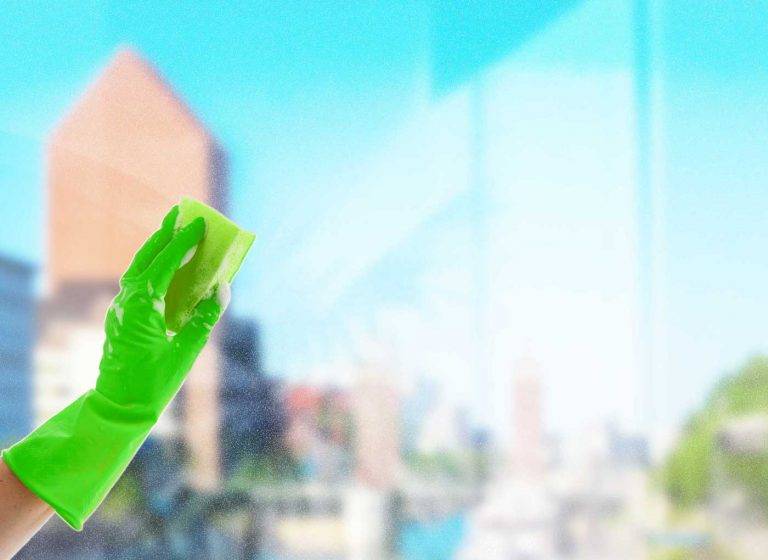 Mitarbeiter von Reinigungskonzepte putzt ein Fenster mit einem Schwamm – im Hintergrund ist grob Duisburg zu erkennen.