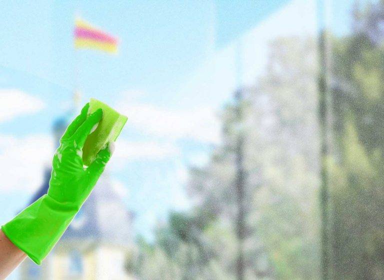 Ein Mitarbeiter von Reinigungskonzepte putzt mit einem Abziehers ein Fenster, durch das man Karlsruher erkennen kann.