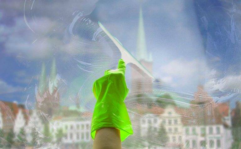 Ein Mitarbeiter von Reinigungskonzepte putzt eine Glasscheibe. Dahinter erkennt man unscharf Lübeck, Schleswig-Holstein.