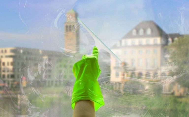 Reinigungskonzepte Mitarbeiter reinigt eine Fensterscheibe mit einem Glasabzieher, mit Blick auf die Stadt Mülheim.