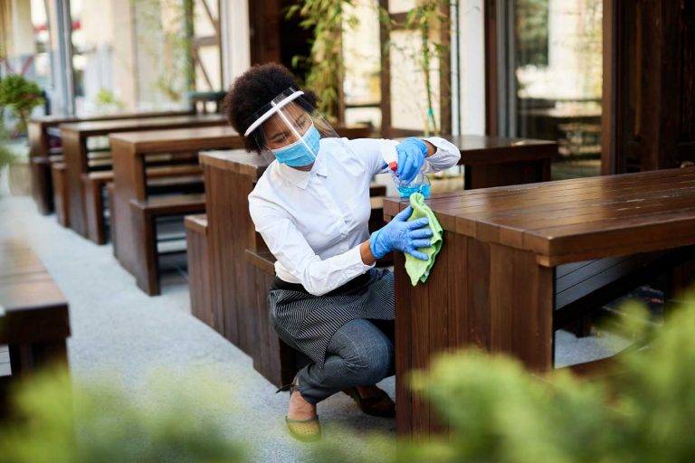Eine Mitarbeiterin von Reinigungskonzepte Dortmund reinigt gewissenhaft die Tische im Außenbereich eines Restaurants.  