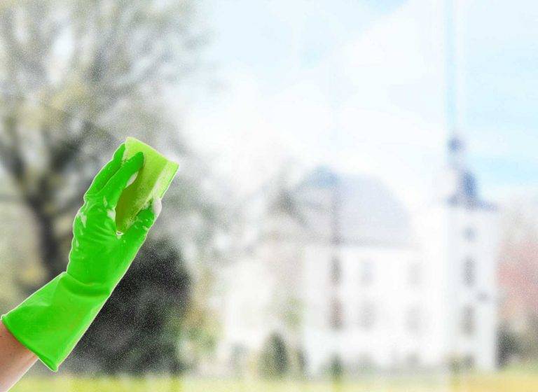 Ein Mitarbeiter von Reinigungskonzepte putzt mit einem Schwamm ein Fenster, durch das man den Ort Voerde erkennen kann.