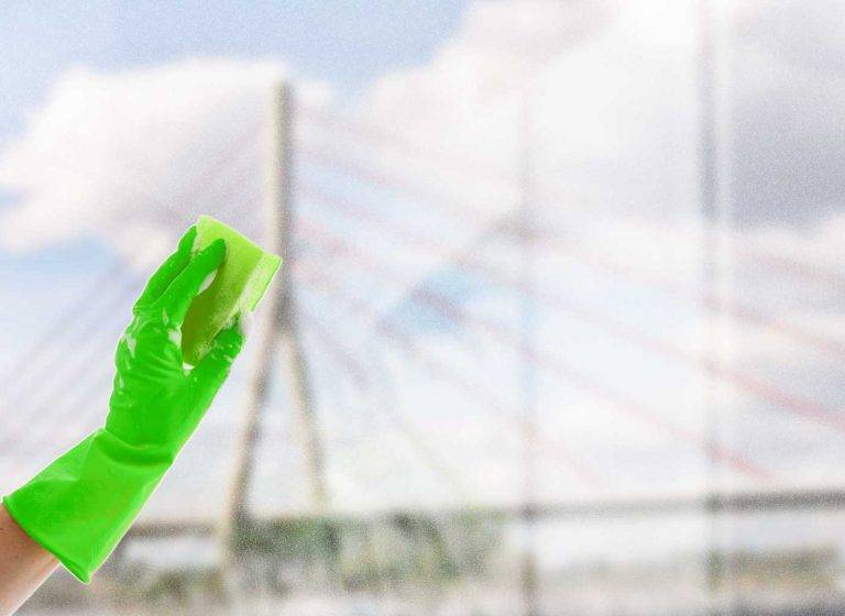 Ein Experte von Reinigungskonzepte putzt mit einem Schwamm ein Fenster. Hinter der Scheibe liegt die Stadt Wesel.