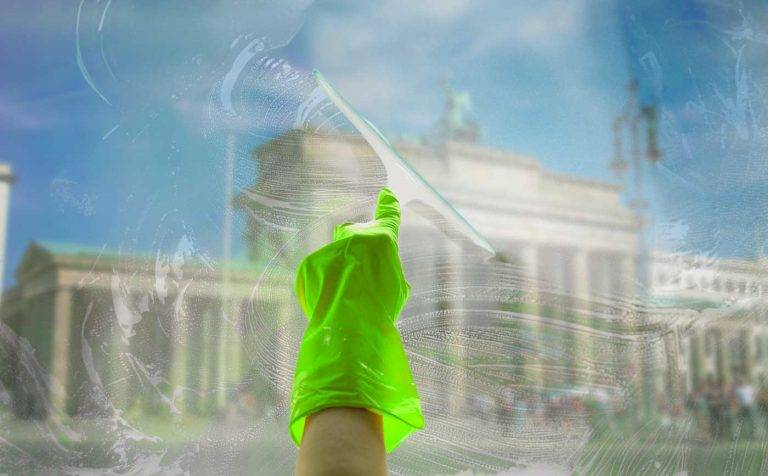 Ein Mitarbeiter von Reinigungskonzepte putzt eine Fensterscheibe. Dahinter kann man unscharf Brandenburg erkennen.