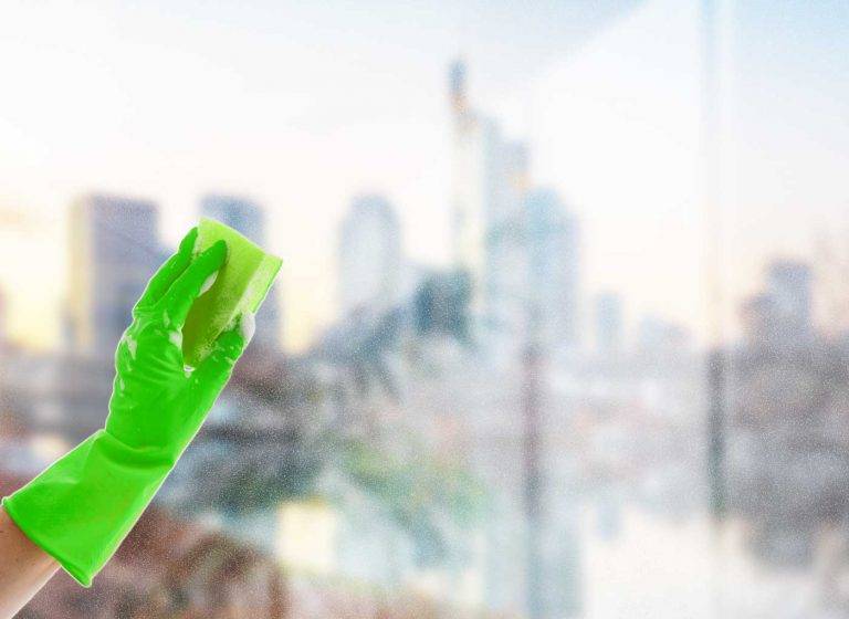 Ein Reinigungskonzepte-Mitarbeiter mit grünen Handschuhen putzt eine Fensterscheibe, dahinter ist Hessen zu sehen.