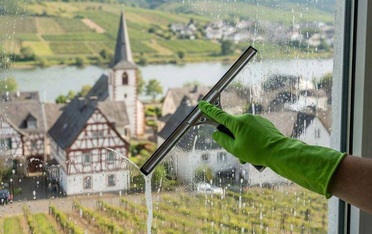 Mitarbeiter reinigt Fenster eines Gebäudes in Oberdiebach mit Blick auf Kirche und Ortskern